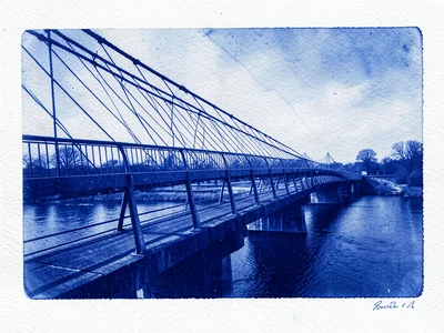 A pedestrian bridge with steel cable railings spanning a river