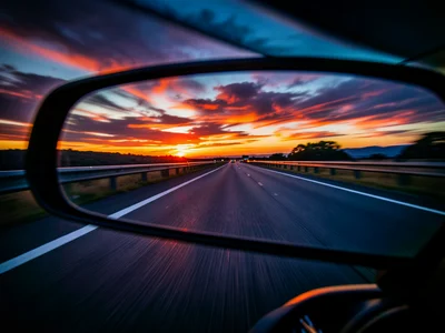 Rear view mirror showing road behind, sunset colors, open highway