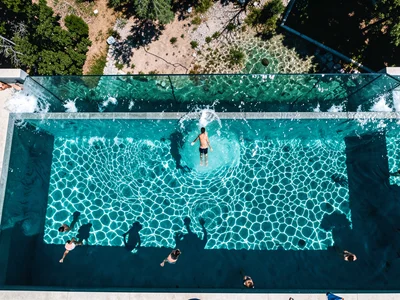 An infinity pool edge from above, the water flowing over into the landscape beyo