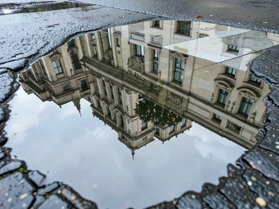 Architectural detail reflected in puddle on marble plaza, ornate building invert