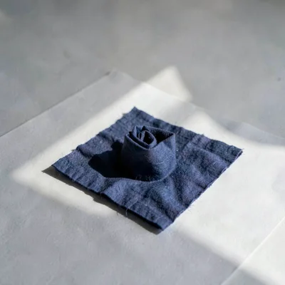 One indigo-dyed napkin folded into a tight square on white-grey paper, fibres so
