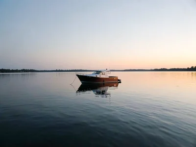 One boat on flat lake at dawn, the water and sky the same silver, floating betwe