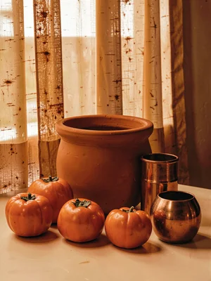 Burnt orange still life, persimmons, terracotta pot, copper vessel, rust light t