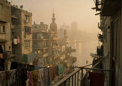 Dusty golden Cairo haze compressing apartment layers, evening call to prayer mom