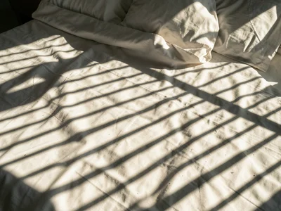 Venetian blind shadows striping across a bed in afternoon light, parallel lines 