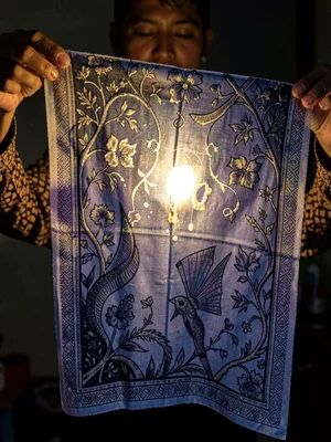 A batik cloth being held up to light — the wax-resist areas glow translucent