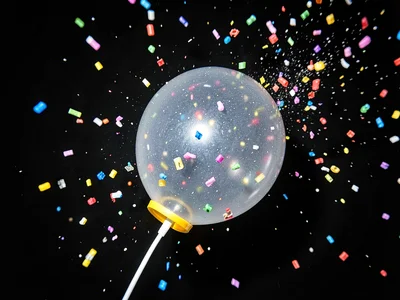 Popping balloon with rubber still retracting and confetti frozen mid-scatter