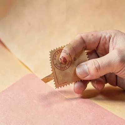 Papercraft hero of a layered paper-cut hand pressing a stamp, warm honey and ros