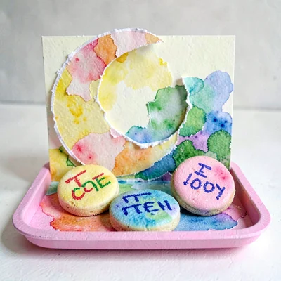 A pop-up paper Eid scene with torn-paper crescent moon and crayon date-cookies o