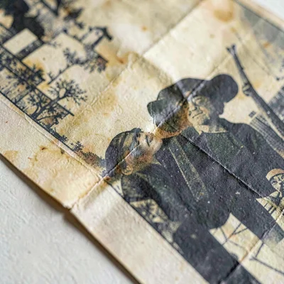 Macro of a folded vintage lithograph poster with deep crease shadows and faded o