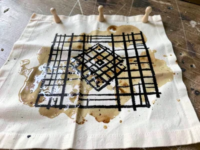 Freshly stamped cloth drying — cloth pegged flat, dye still wet and gleaming