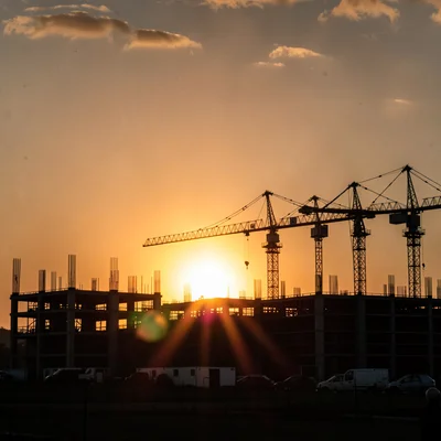 Construction site cranes silhouetted against warm orange horizon