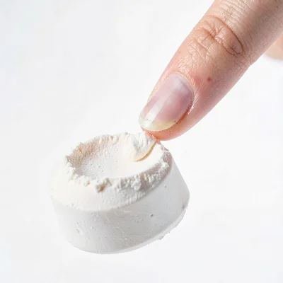 Clean studio macro of a perfectly pressed powder cake breaking under a fingertip