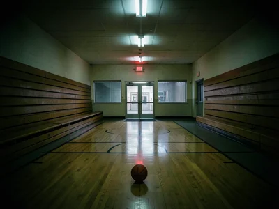 A school gymnasium at night lit only by the exit signs and the glow from the hal