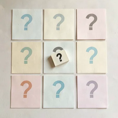 Overhead 3x3 grid of nine pastel question cards on cream paper, one tile lifted 