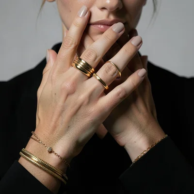 Close-up of hands wearing stacked gold rings and bracelets, neutral manicure, mi