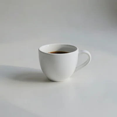 Minimalist photographic still life of a single white coffee cup on a clean matte surface, soft natural window light, gen