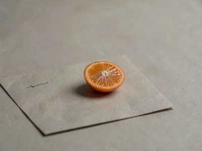 One slim half of a kumquat laid cut-side up on warm-grey paper, segments tiny an