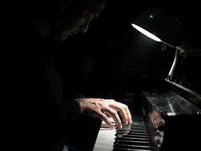 Pianist hands on keys, practical lamp on piano the only light, keys alternating 