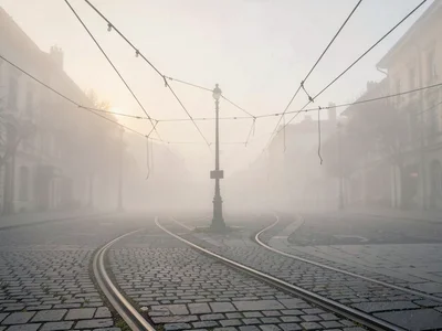 Tram tracks curving across an empty plaza in dawn fog, overhead wires drooping i