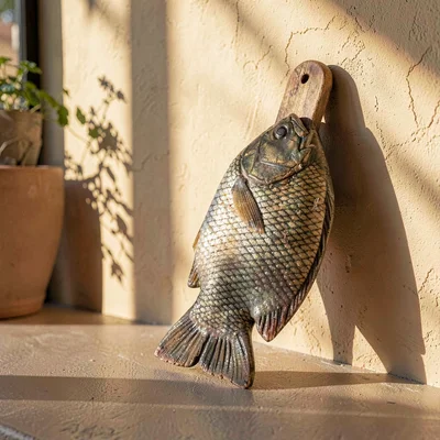 Product still life of a fish-tail board leaning against a sun-warmed wall