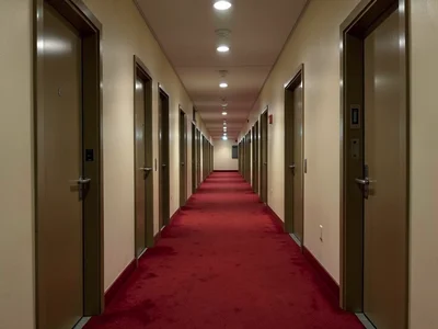 Long hotel corridor in deep perspective, identical doors both sides, red carpet,