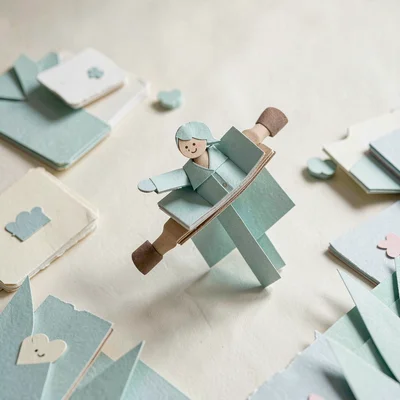 Papercraft hero of layered paper task cards drifting across a paper field, soft