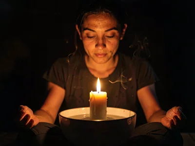 Candle floating in bowl at meditation, face barely visible in dark, the inner li