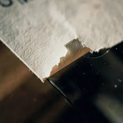 Tight texture study of a hand-pressed paper label peeling at the corner against