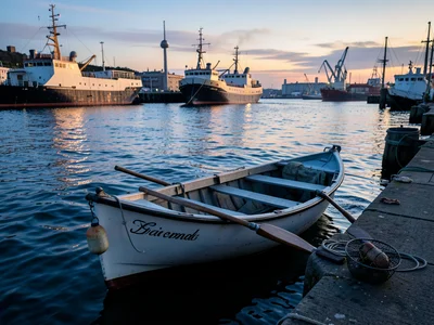 A rowing dinghy tied to a pier, gentle waves rocking it, oars shipped, a crab po