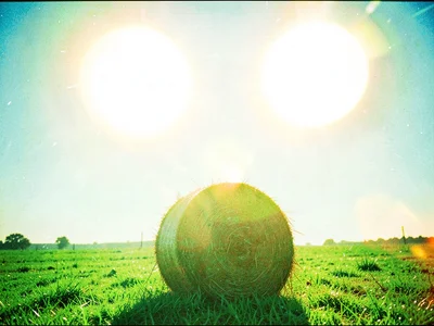 Two suns hanging side by side above a single round haybale alone in a field of g