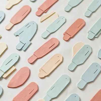 Papercraft pattern of repeating paper-cut markers in soft sage, coral and butter