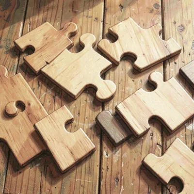 Warm flat-lay of mixed wooden puzzle pieces on a worn wooden surface, soft cast