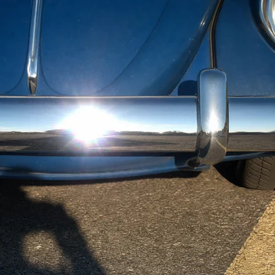 > A chrome bumper of a 1968 Beetle photographed at close range, the bumper filling the central horizontal band of a squa