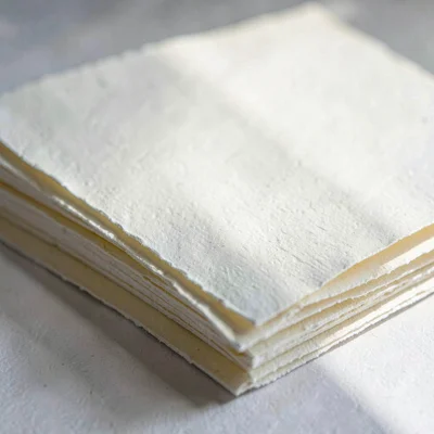 Paper macro of a stack of cream printmaking sheets with deckle edges, raking sid