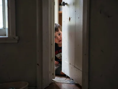 Child hiding behind half-open closet door, eye visible in the crack, the doorway