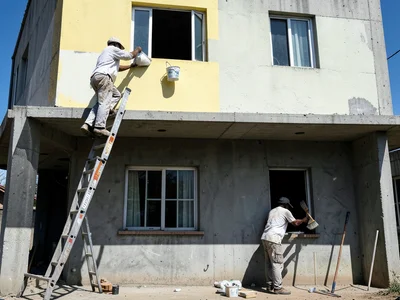 A house painter on a tall extension ladder painting the fascia board of a two-st
