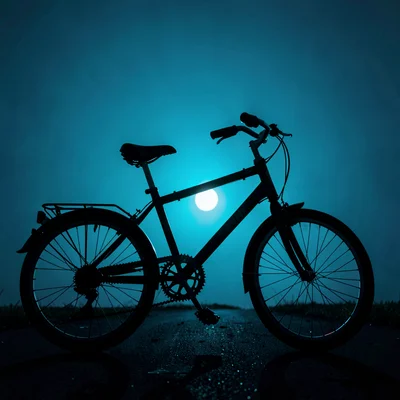Nocturnal photo of a single spin bike silhouetted against a deep cyan back-glow,
