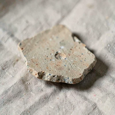macro of a chipped pottery shard on neutral linen, mineral-cut detail