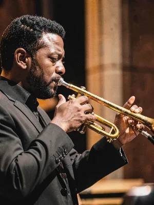 A jazz musician in profile playing trumpet, bell and fingers telling everything