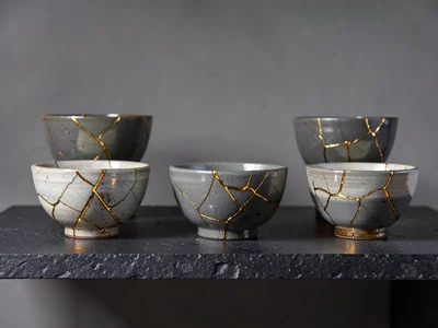 Collection of five repaired bowls on dark stone shelf — varying crack patterns