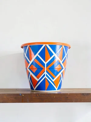 Painted decorative pot on shelf — geometric band, electric blue and orange on wh