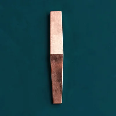 sleek triangular bookmark in copper foil straight-on against a deep teal backdro