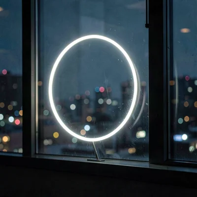 Nocturnal shot of a ring light reflected in a darkened window, city blur beyond
