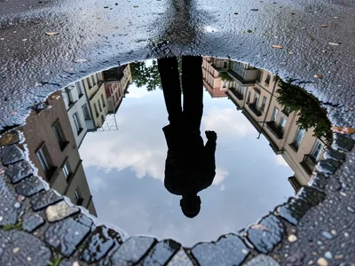 Passing figure reflected as silhouette in street puddle, person walking inverted