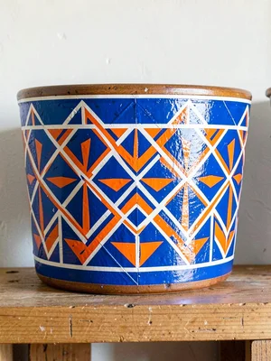 Painted decorative pot on shelf — geometric band, electric blue and orange on wh