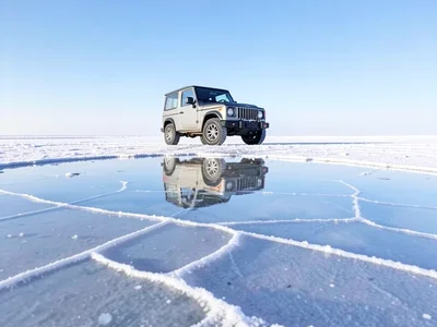 Vehicle parked on salt flat — small 4x4 with the entire sky mirrored beneath it