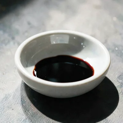 A small porcelain dish with a slow black puddle of balsamic catching one hard ri