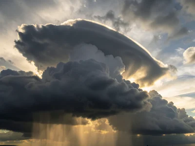 Storm cell backlit by late sun — dark grey anvil cloud with golden edges and rai