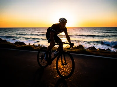 Cyclist riding along a coastal road at sunrise, silhouetted against the ocean